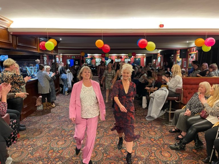 Two women walking down the catwalk during the fashion show.