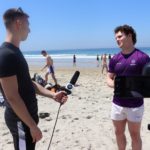 A man (Oliver Mould) interviewing another man (Alex Green) on a beach
