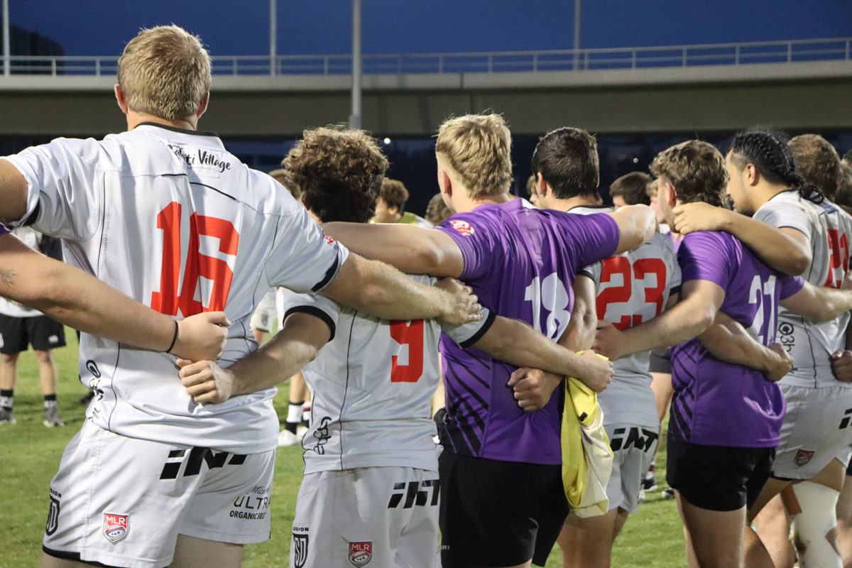 An image of different rugby players in purple and white tops with their arms behind eachother bags
