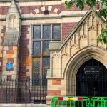 Image shows the entrance to Leeds University building, The Great Hall. Orange paint is splashed across the windows to the left of the entrance and green barriers have been placed to block the buildings entrance.