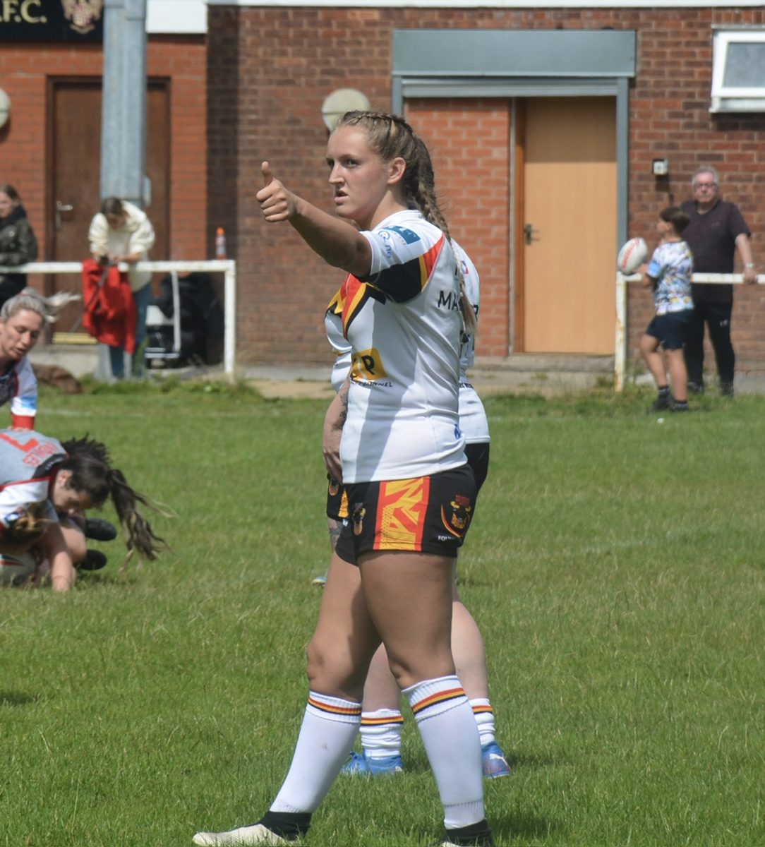 A girl in a white top and black shorts posing with her thumbs up.