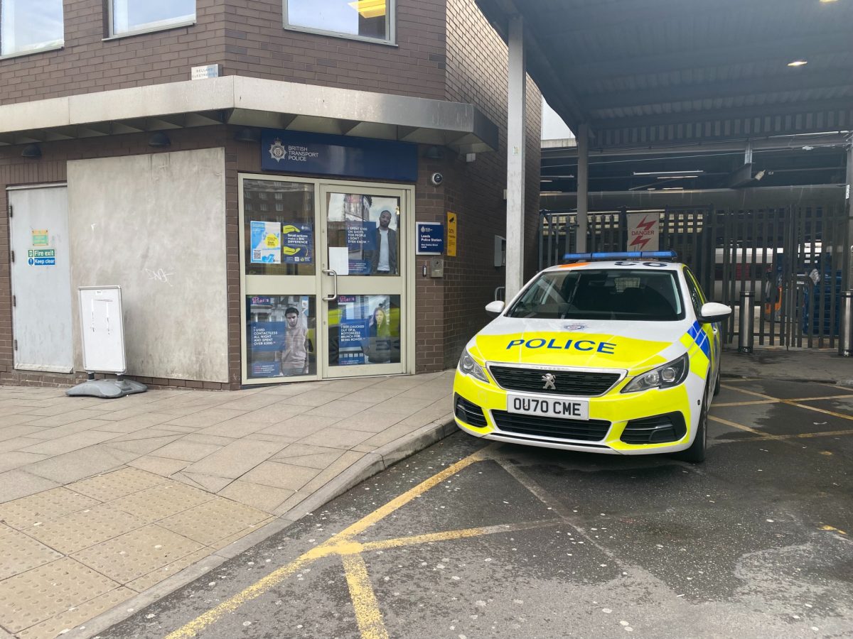 The image shows a police car parked next to the entrance for the British Transport Police Station in Leeds. The car is decorated with neon police vinyl.