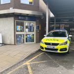 The image shows a police car parked next to the entrance for the British Transport Police Station in Leeds. The car is decorated with neon police vinyl.