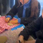 two girls drawing arounnd stensils on fabric to make reusable sanitary pads