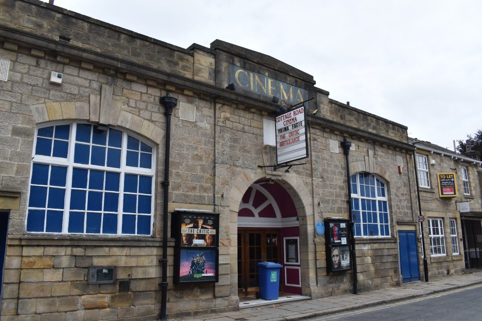 This is an image of the outside of Cottage Road Cinema. It has sand-coloured brickwork and large opaque windows either side of the entrance which have been painted blue. This building has quite an old-fashioned feel.