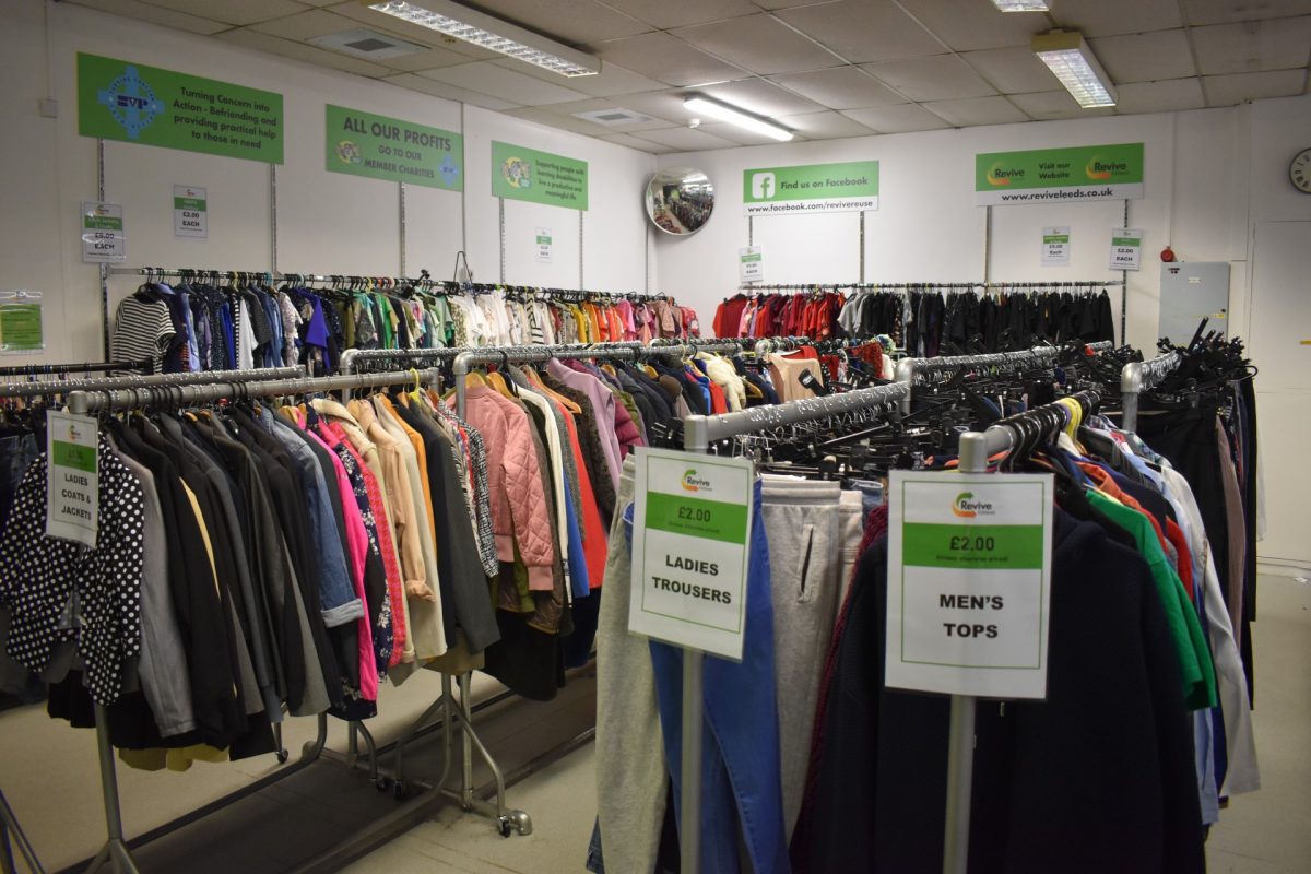 Clothing racks inside the Revive Reuse shop, in Kirklees. There are green signs on the walls behind.