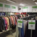 Clothing racks inside the Revive Reuse shop, in Kirklees. There are green signs on the walls behind.
