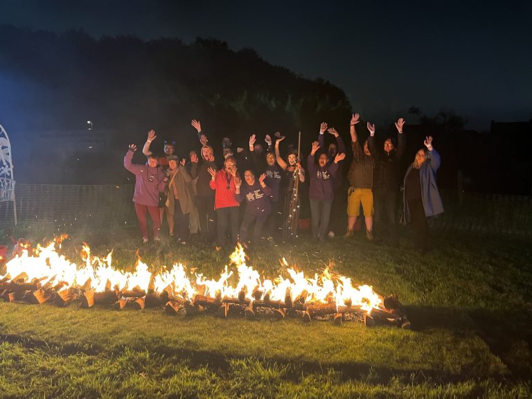 A group of people who are stood infornt of a fire bed cheering after completitng their fire walk