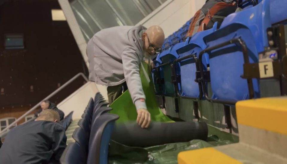 A man who is stood in the stand of Headlingley stadium rolling out a sleeping mat as he sets up his bed for the night