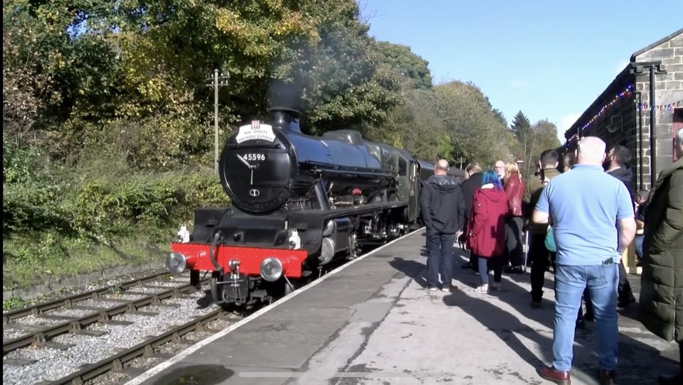 A black steam train pulling into Keighley Railway station as guest of the beer and music festival wait to be taken to the other locations