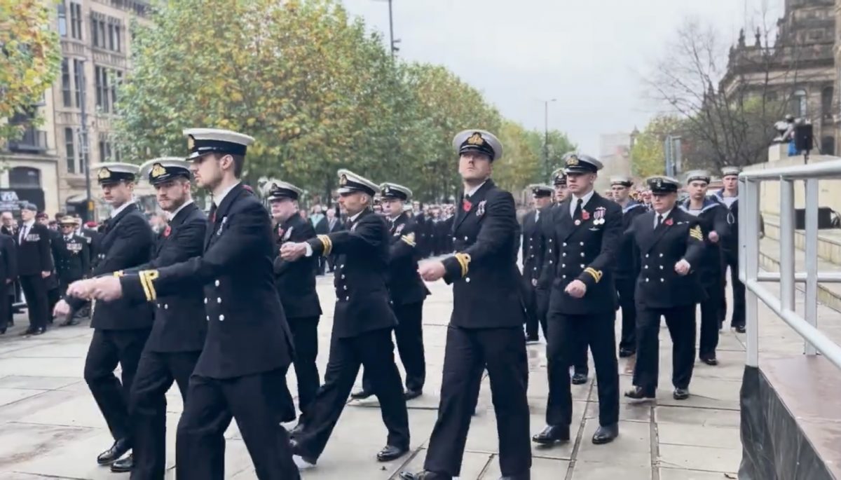The image shows members of the navy marching out of the cenotaph following the Remembrance Sunday service. The group are marching in sync all in their naval uniform