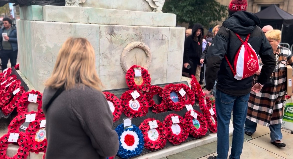 In this image, people can be seen looking at the poppies wreaths that have been laid by the cenotaph.