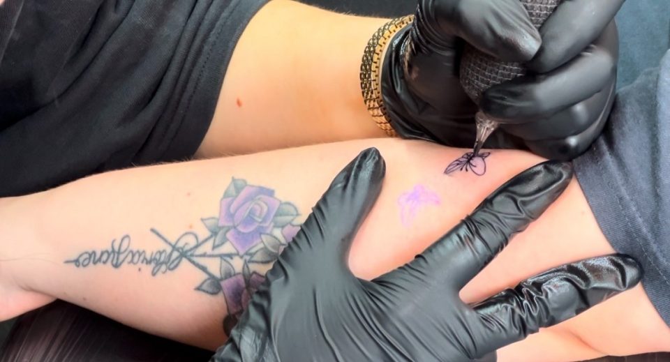 This is a close up image of a tattoo artist inking somebody's arm. They appear to be doing a butterfly design