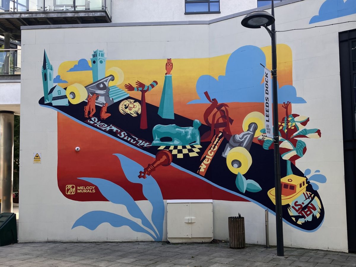 This image features a colorful mural on a wall, showcasing a dynamic and abstract design. The mural includes elements such as a skateboard, distorted clock faces, buildings, and figures in motion, along with whimsical touches like clouds and plants.