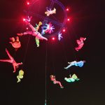 The image shows a number of acrobats performing in the sky attached to a crane