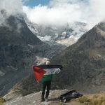 Man holding green, red, black and white flag in support of Palestine in front of mountains