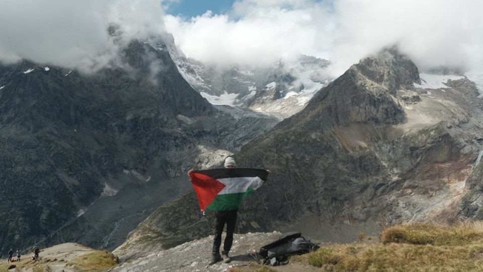 Man holding green, red, black and white flag in support of Palestine in front of mountains