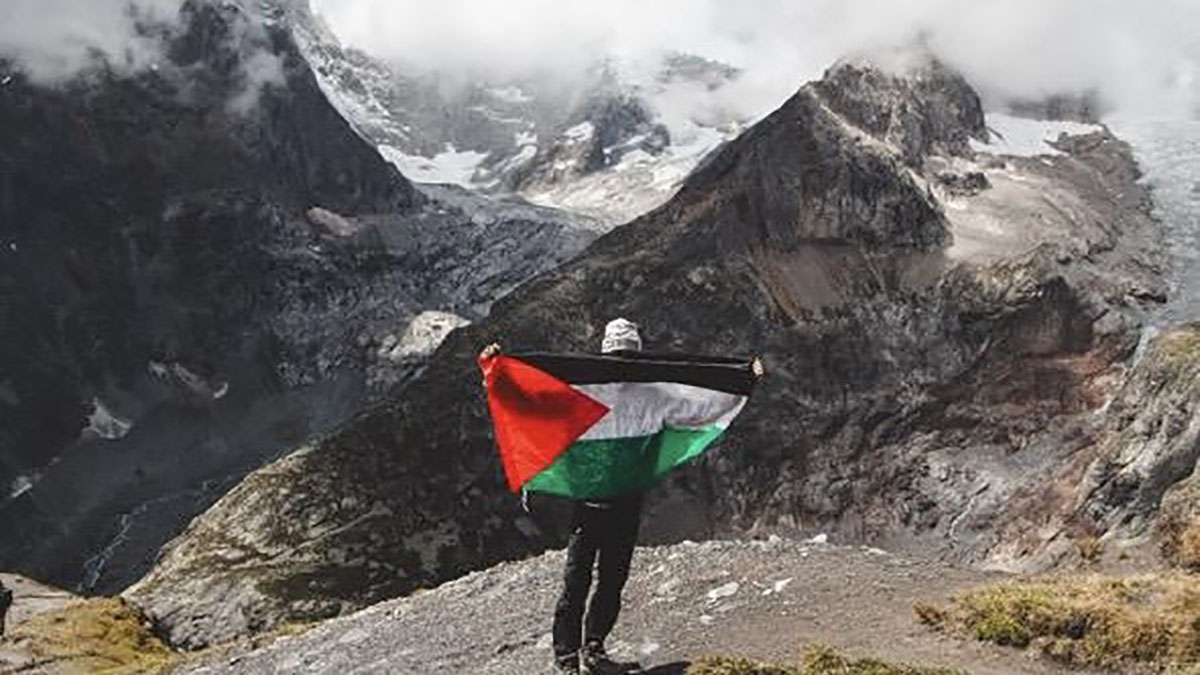 man holding green, red, black and white flag in support of Palestine stood in front of mountains