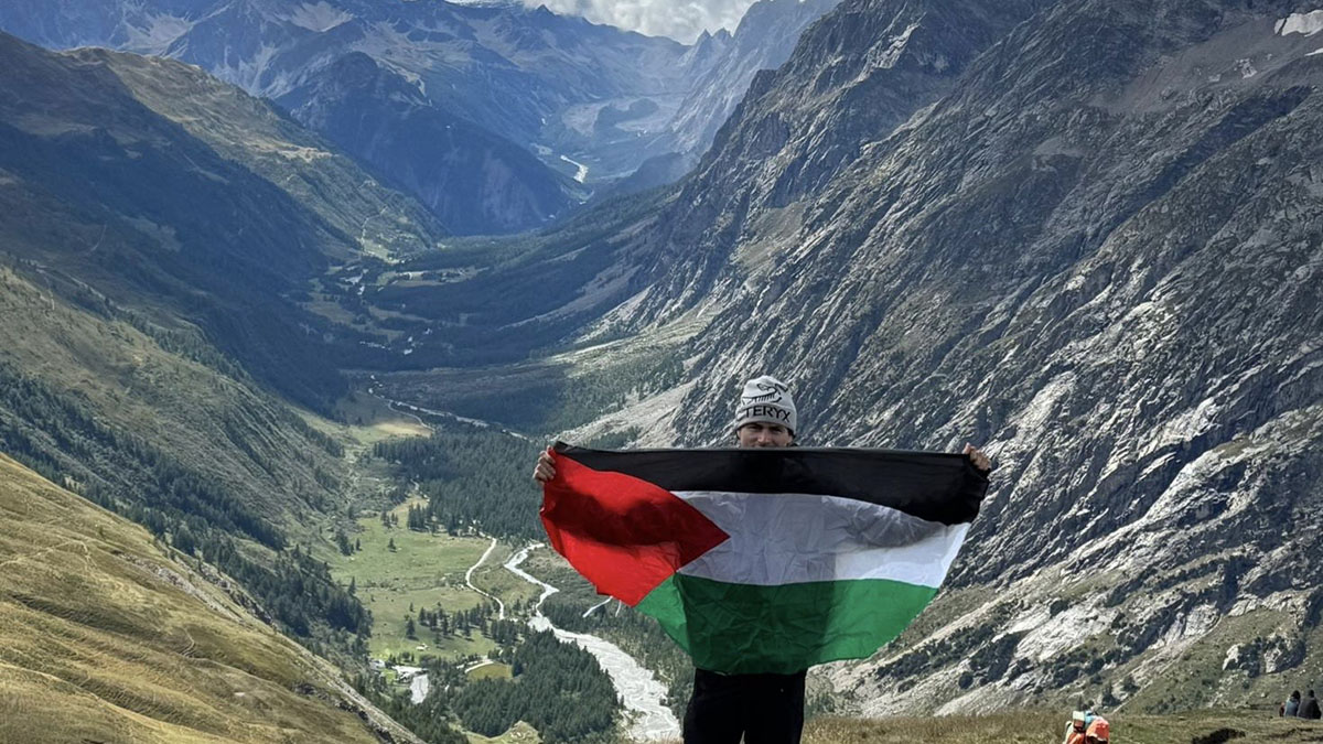 Man holding green, red, black and white flag in support of Palestine infront of mountains