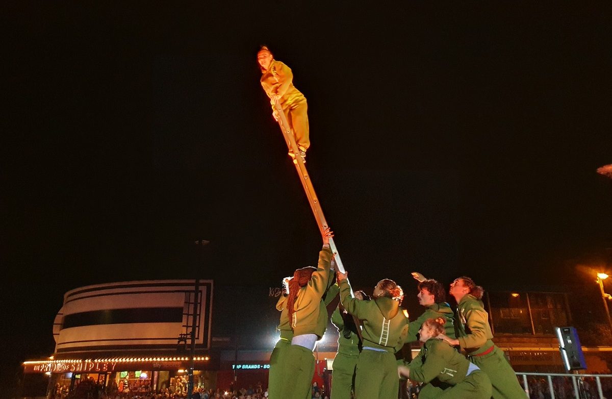 The image shows performers doing stunts on ladder in Shipley at night
