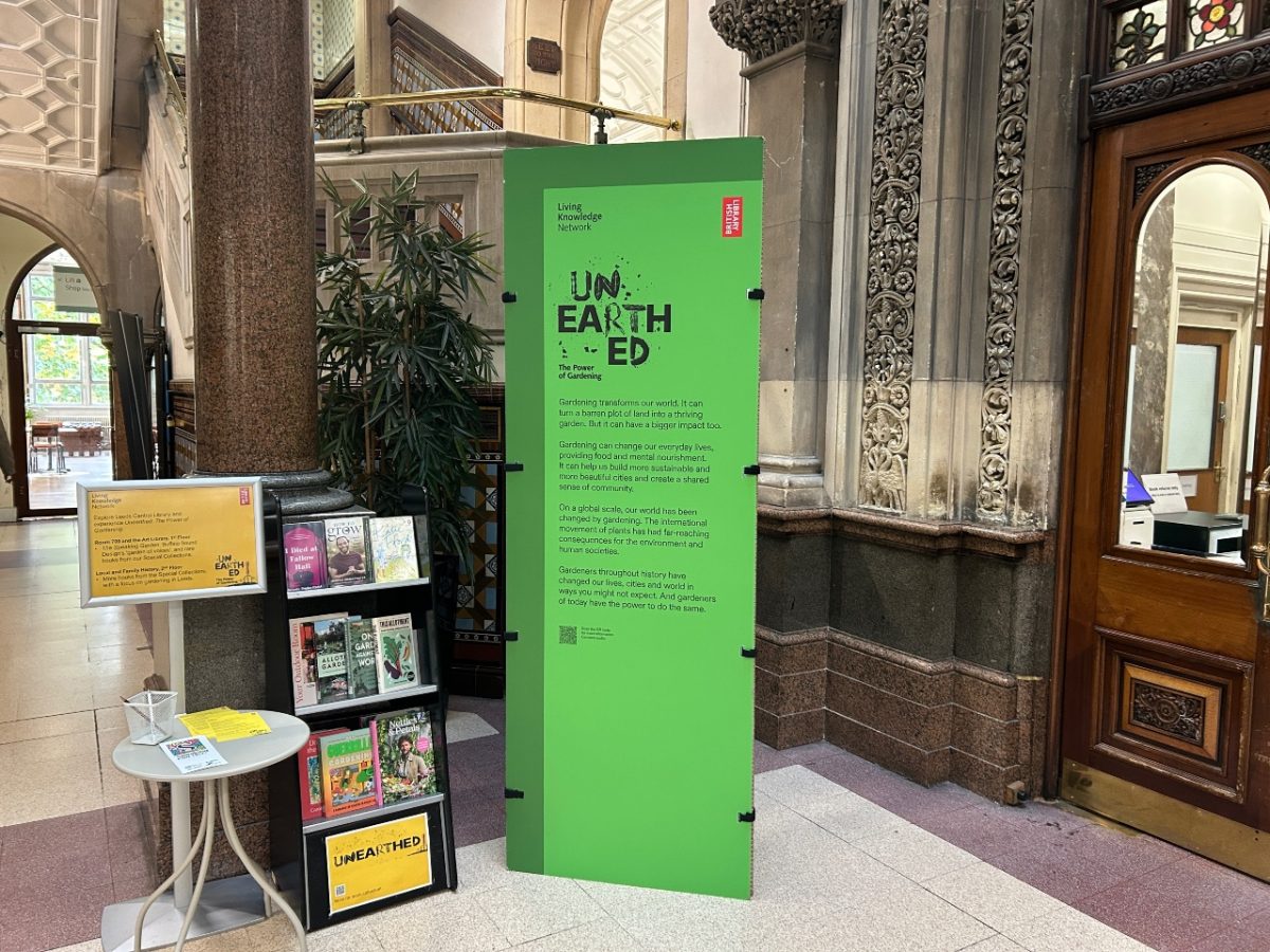 a green banner stood in an old building with tile flooring and intricately carved stone wall. The banner features black writing that explains what the exhibition is.