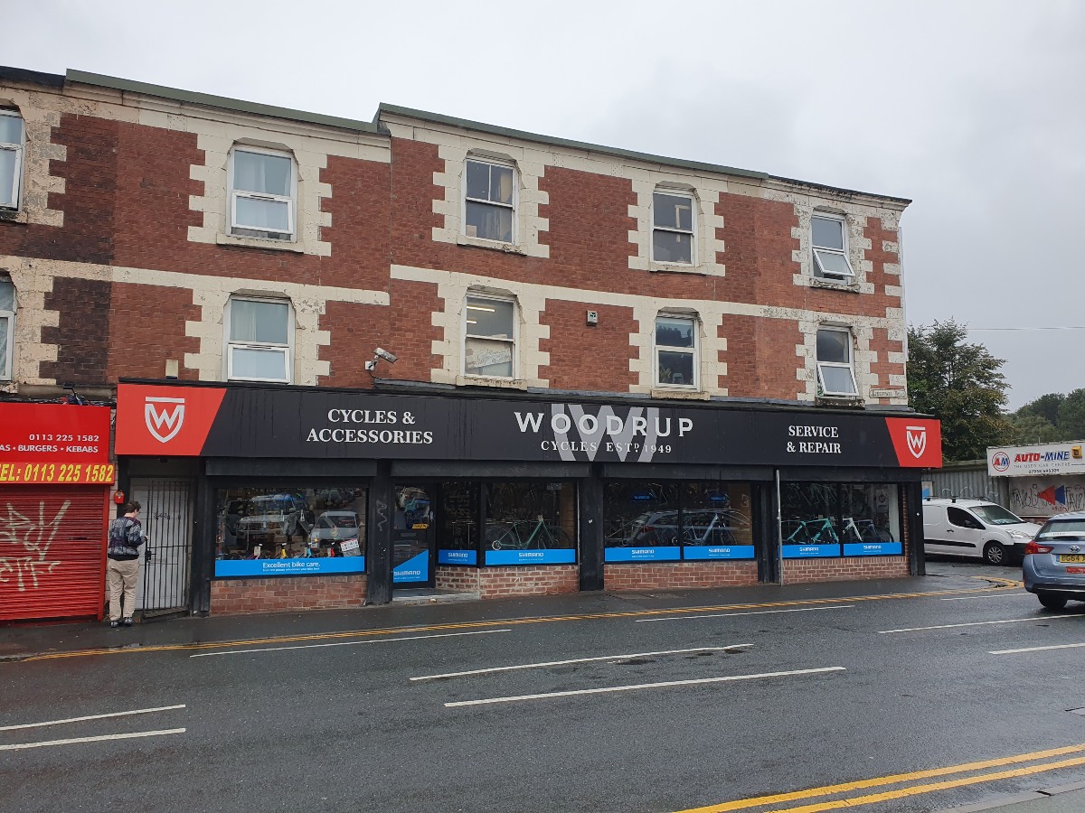The image shows woodrup cycles on Kirkstall road on a rainy day with cars in the background