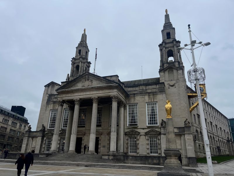 Neoclassical building with twin towers and columns, featuring a golden owl statue in front under an overcast sky.