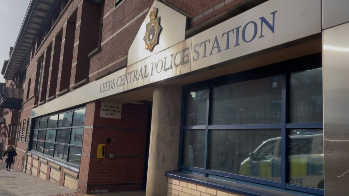 Exterior of Leeds Central Police Station on a sunny day, showing the building’s brick façade, police signage, and reflection of a police vehicle in the window.