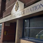 Exterior of Leeds Central Police Station on a sunny day, showing the building’s brick façade, police signage, and reflection of a police vehicle in the window.