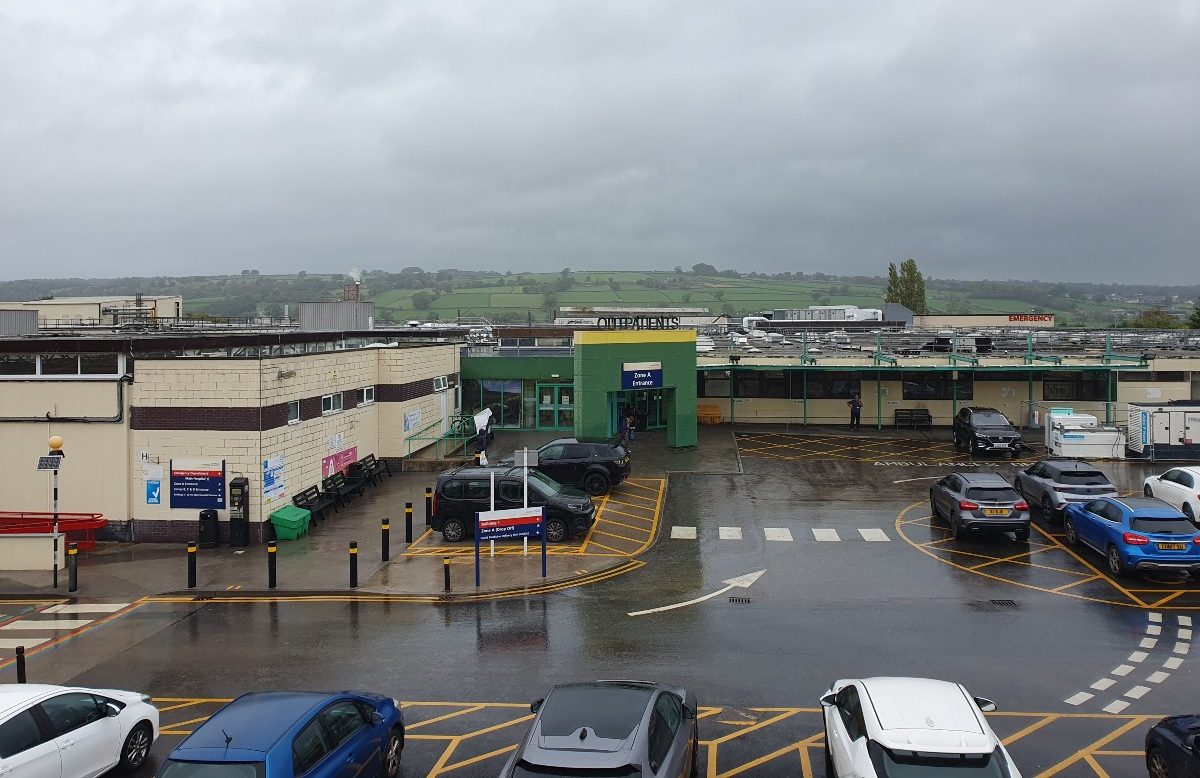 The image shows the entrance to Airedale hospital with clouds and fields in the background