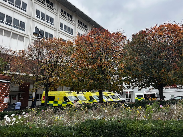 several yellow and green emergency ambulances parked outside a hospital building