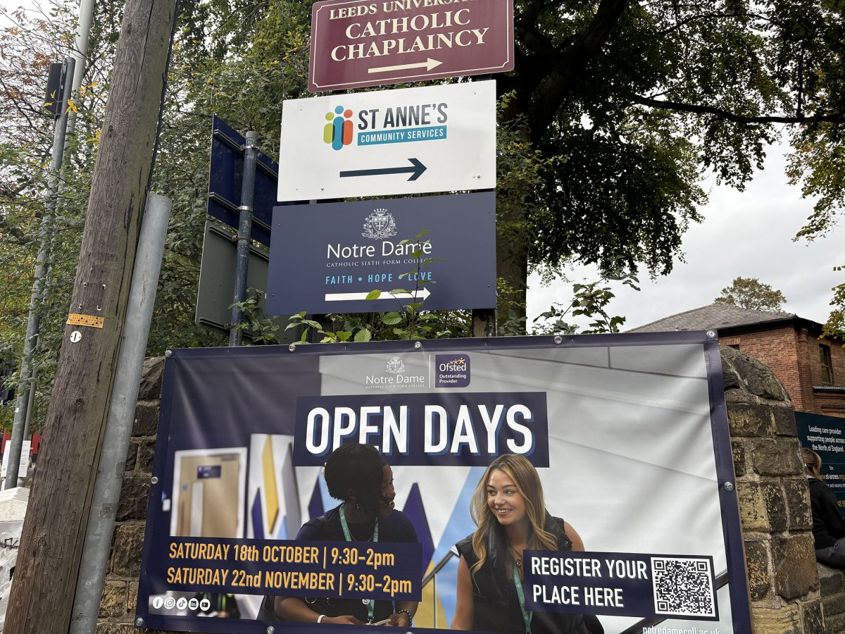 Signs near trees show "Leeds University Catholic Chaplaincy," "St Anne's Community Services," and "Notre Dame College." A banner promotes Notre Dame College open days.