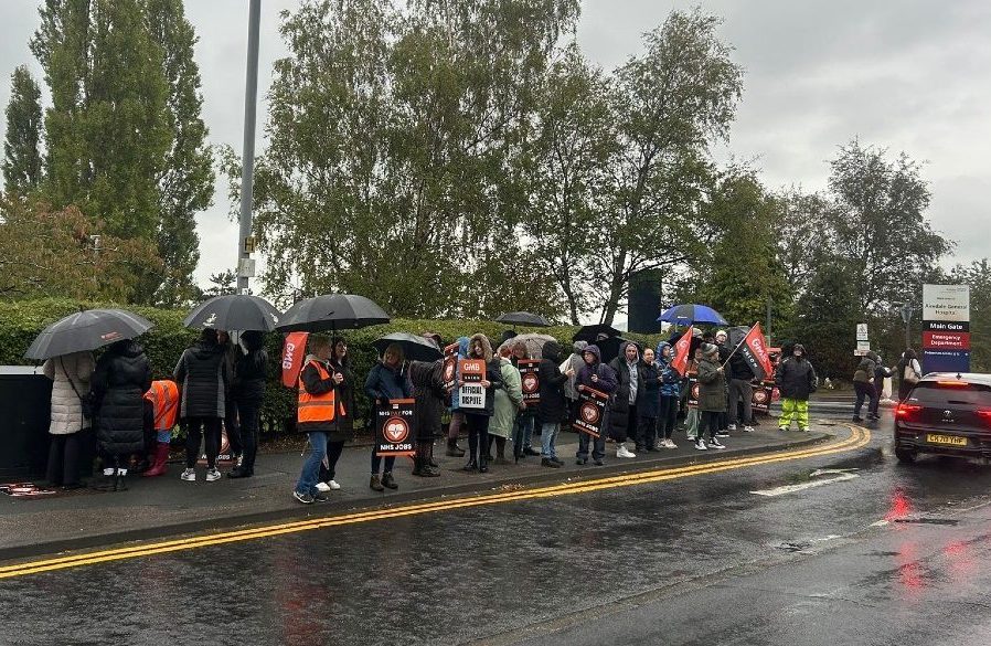 The image shows the GMB union picket line in the rain outside Airedale Hospital