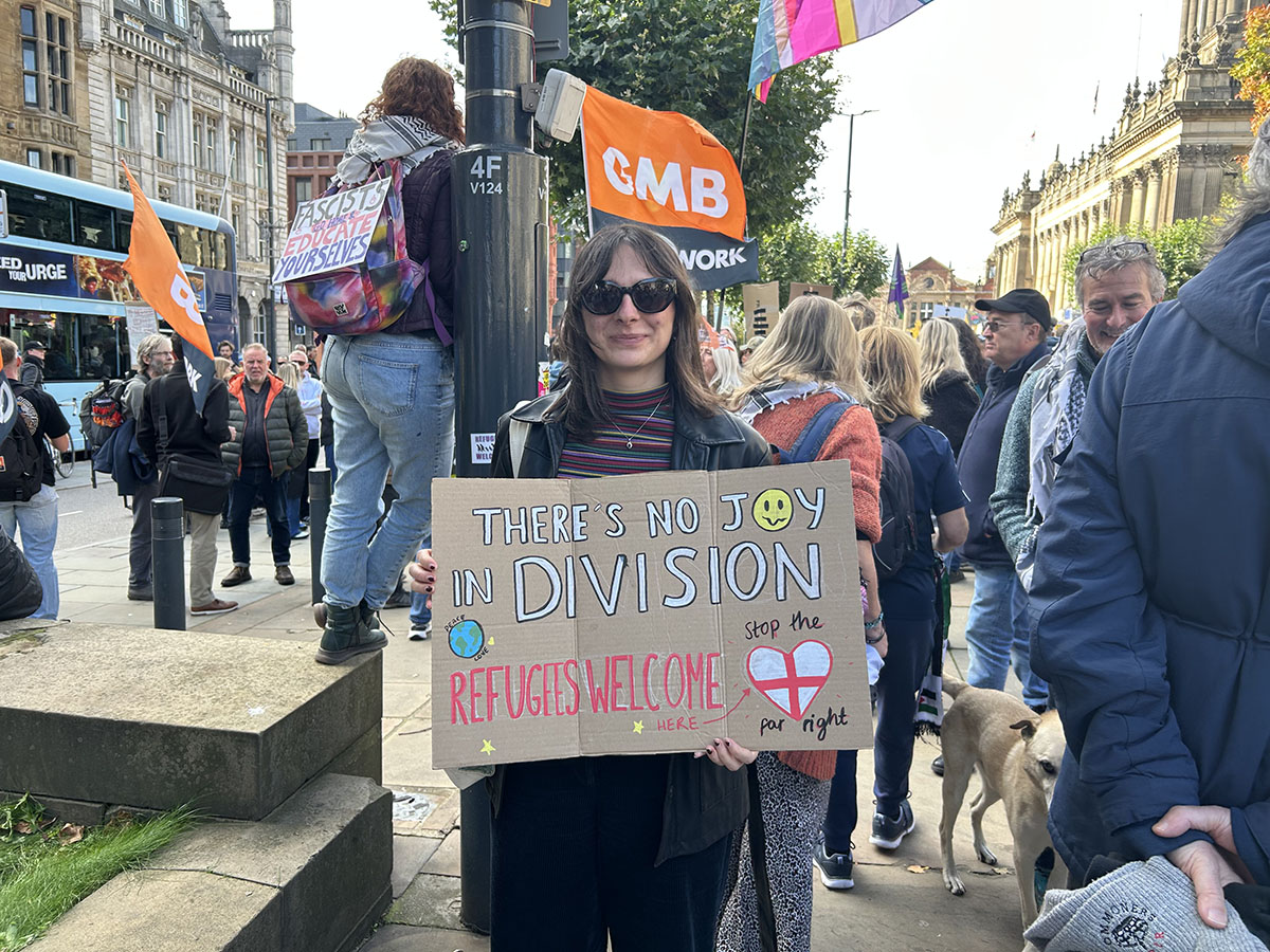 Woman holding sign saying "there's no joy in division. Refugees welcome here. Stop the far right."