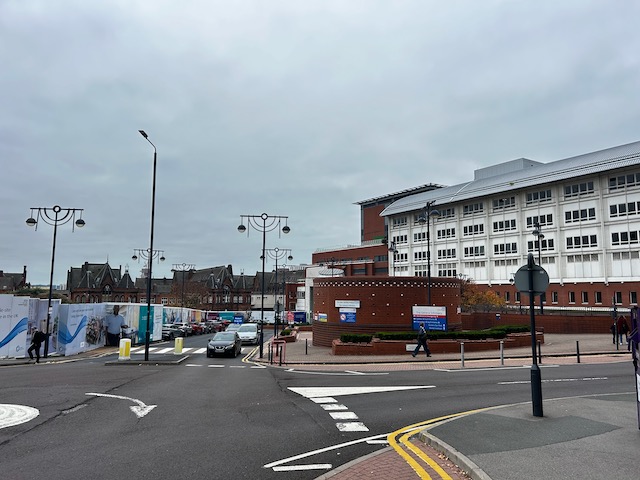 Street view outside a hospital in Leeds, with a large white and red building in the background