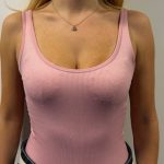 person wearing a pink ribbed tank top and dark jeans, standing against a plain white wall