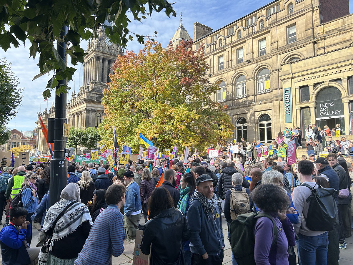 People gathered in a crowd before protest, signs and flags flying high.