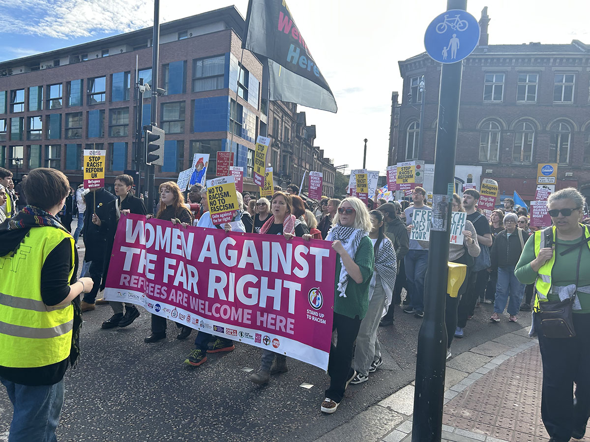 women walking whilst holding large pink banner saying "women against the far right"