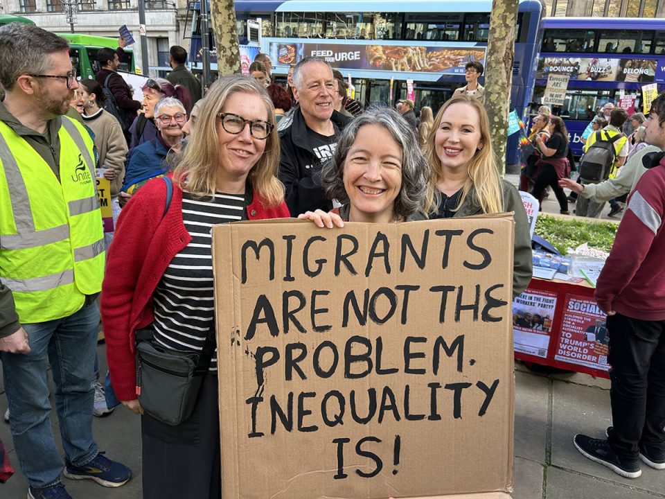 Three women holding cardboard sign saying "migrants are not the problem. inequality is!" in capital letters