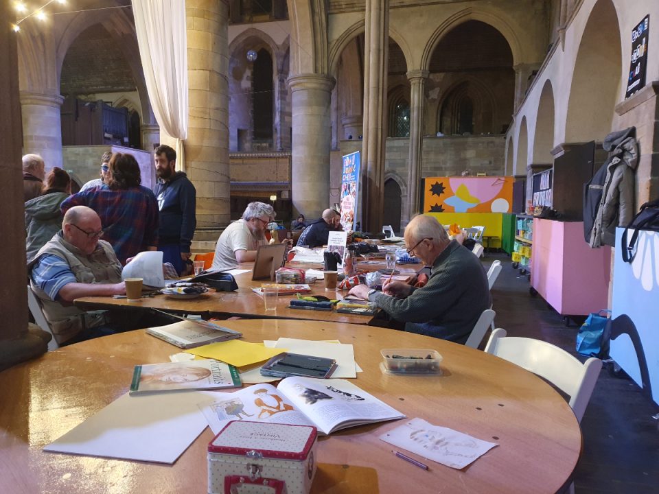 The image shows people round a table drawing in a church