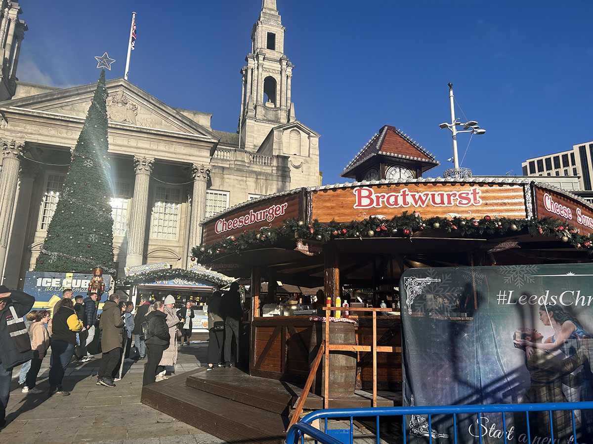 Image of people queueing for Bratwurst stall at Christmas markets, infront of a large christmas tree and town hall.