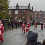 Runners dressed up as Santa are caught in action running down a rainy street.