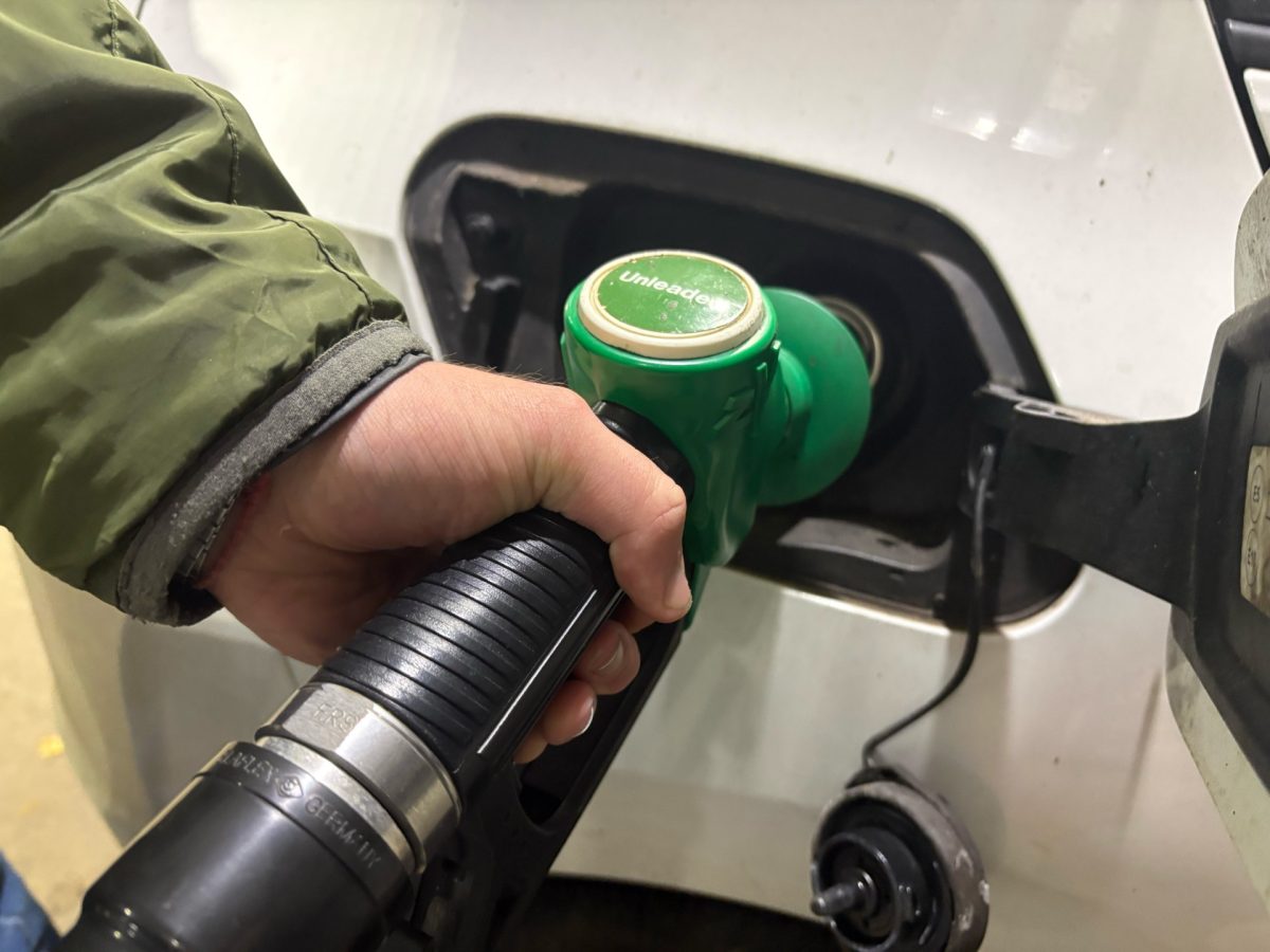 Close-up of a person holding a green fuel nozzle inserted into a vehicle’s fuel filler opening at a petrol station.