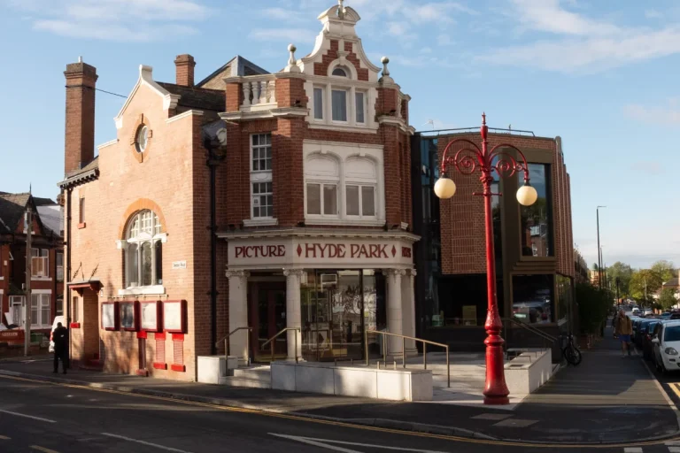Exterior view of the historic Hyde Park Picture House building with red brick features, white decorative gables, and a bright red lamp post in front.