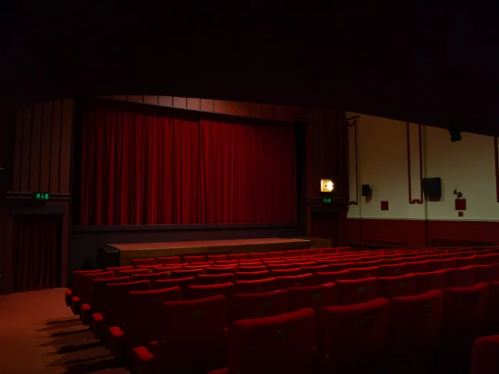 Cinema auditorium view facing a closed red stage curtain and rows of red velvet seats.