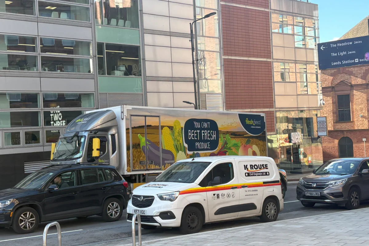 A delivery lorry displaying fresh produce on a busy street.